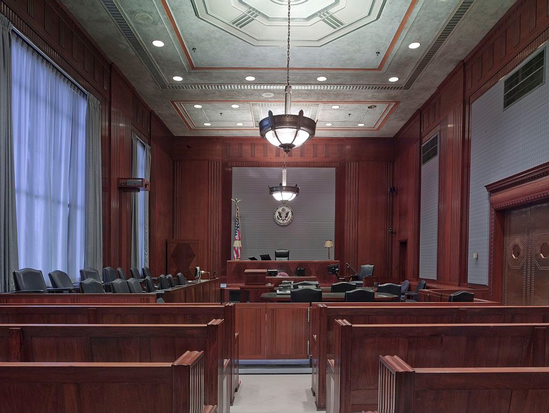 Interior of an empty courtroom showing judge's bench, witness stand, jury box, and spectator seating for a mediated divorce hearing. American flag and state seal are visible in the background.