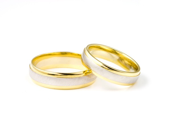 Two wedding bands on a white background; one is gold and the other is silver with a spousal support band in the middle.