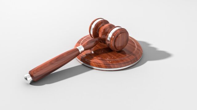 A wooden judge's gavel lies on a sound block, both featuring polished surfaces with visible wood grains, set against a plain light gray background. This image symbolizes the legal decision-making in domestic violence