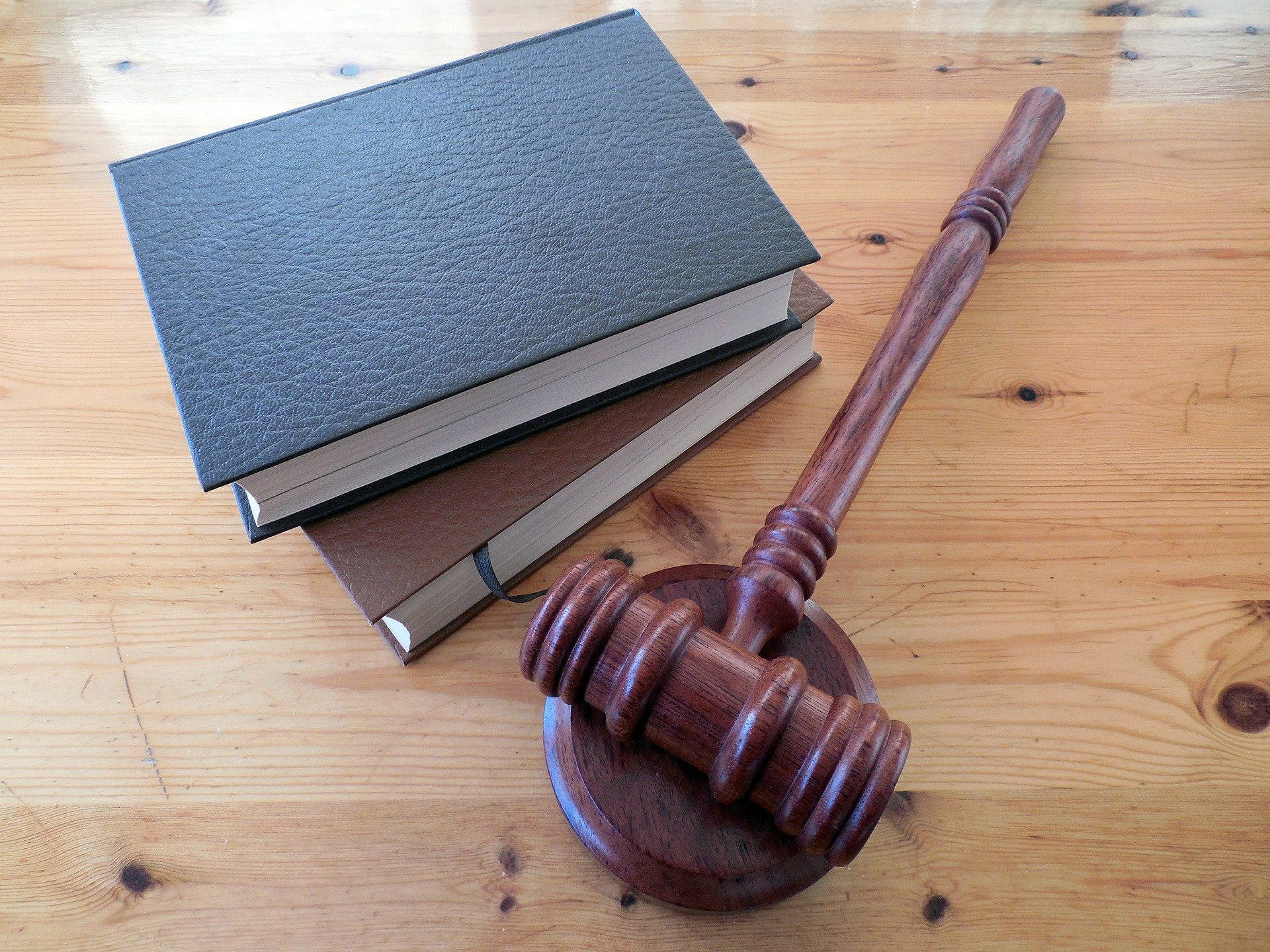 A wooden gavel rests on top of three stacked hardcover books on a wooden table, symbolizing legal concepts related to domestic violence.