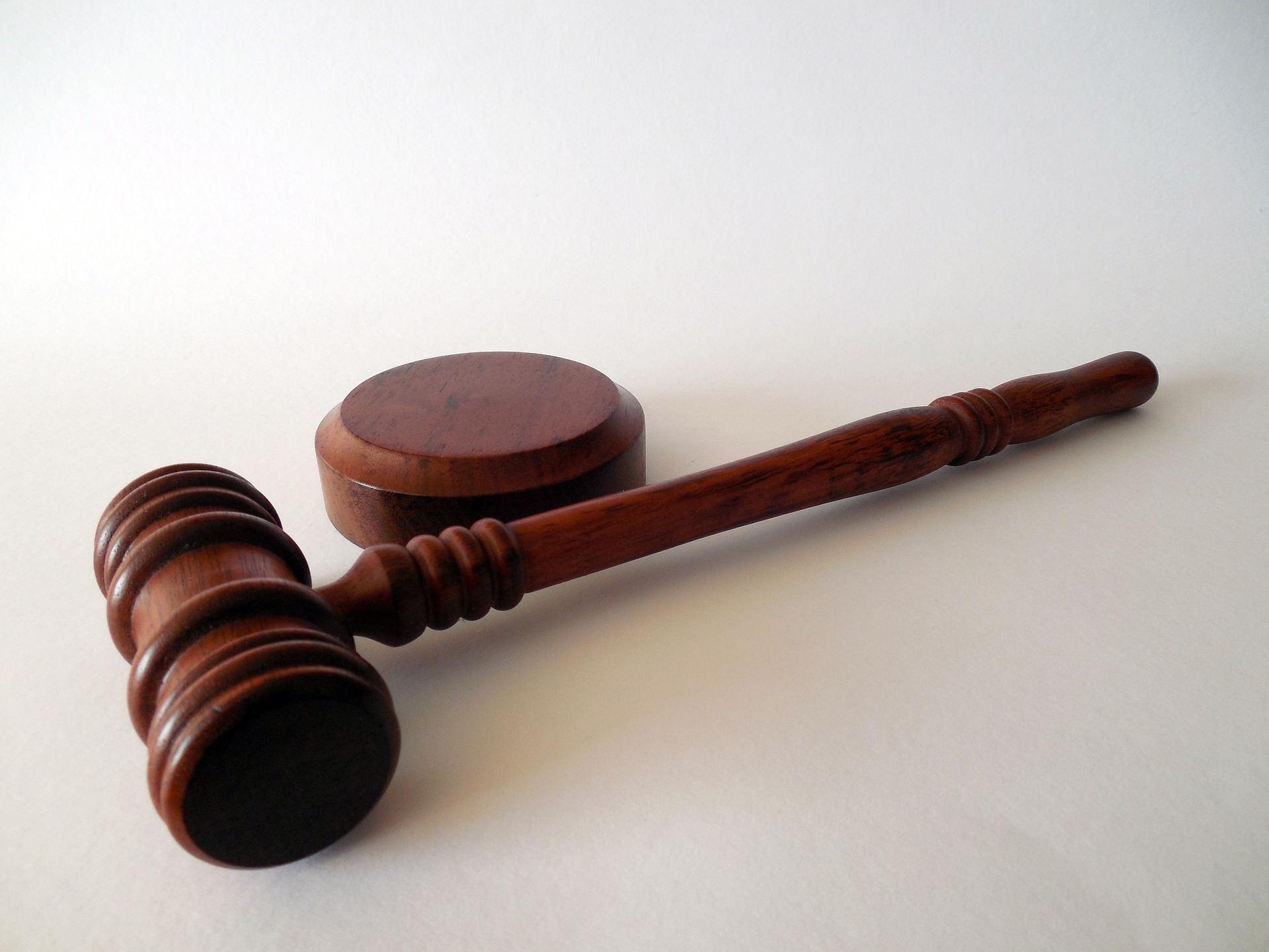 A wooden gavel resting on a white surface, angled to show its head and handle, typically used by judges or at auctions to address acts such as domestic violence.