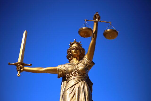 A golden statue of lady justice holding a sword and scales against a clear blue sky, symbolizing fairness and legal integrity in cases of domestic violence.