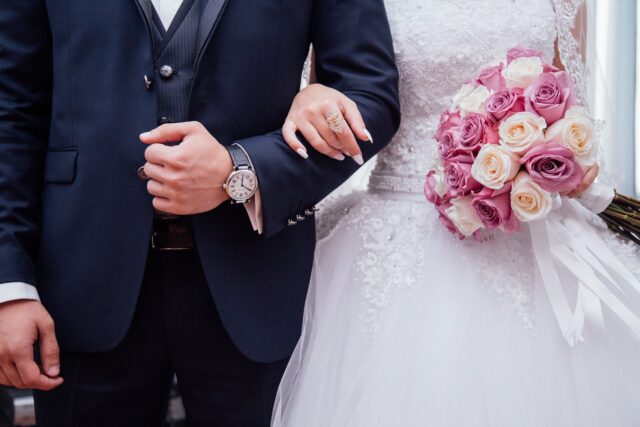 A close-up view of a bride and groom, focusing on their torsos. The bride holds a bouquet of pink and white roses, symbolizing the blending of lives through their prenuptial agreement
