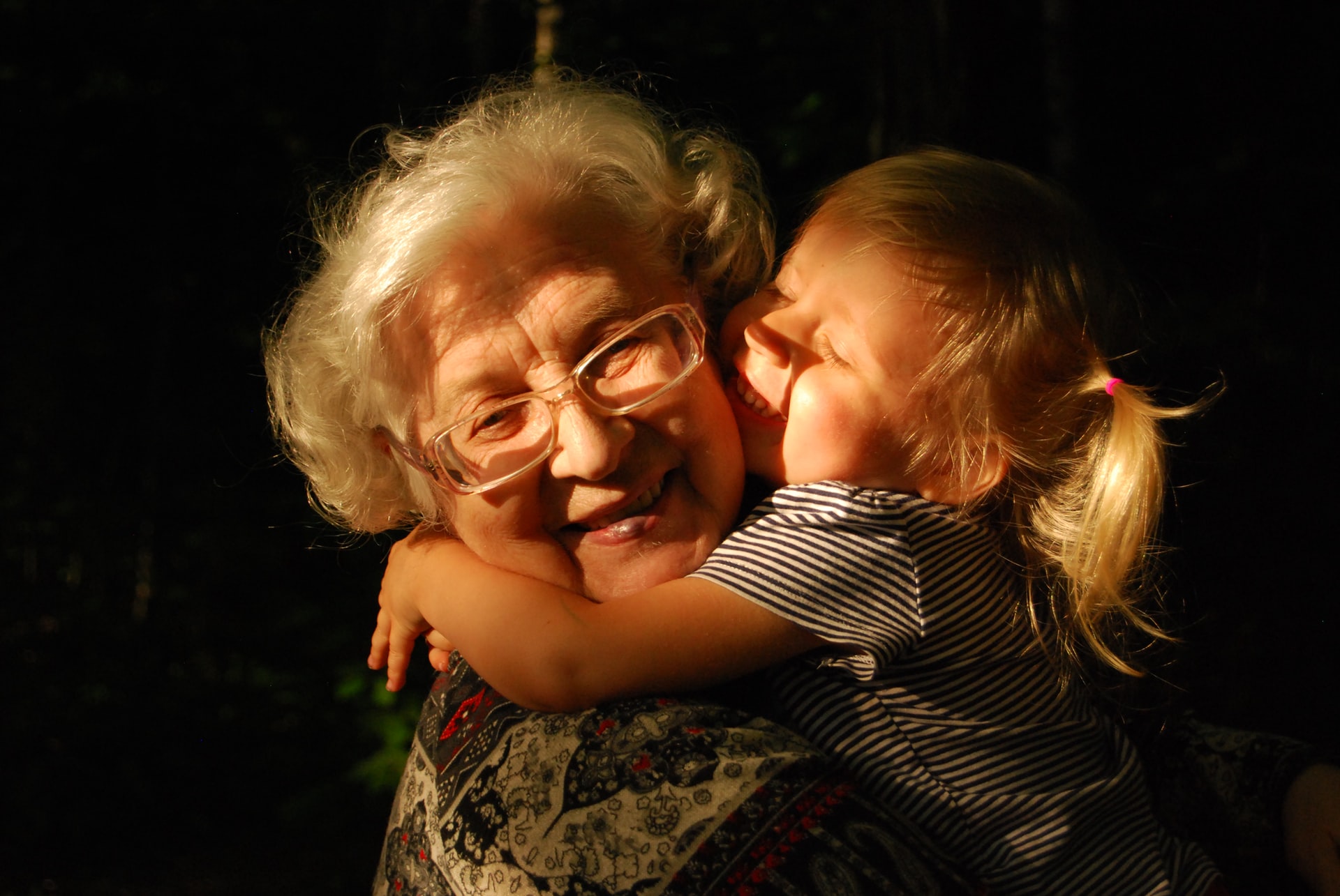 An elderly woman with glasses and a young girl hugging joyfully in a sunlit forest setting, expressing affection and happiness, embodying the essence of grandparents' rights.
