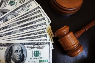 A wooden gavel lies next to a stack of US hundred-dollar bills on a dark surface, symbolizing the intersection of law and finance in the context of New Jersey alimony.