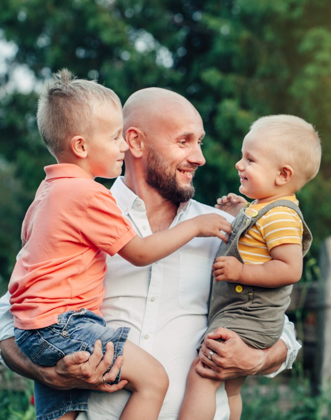 Father holding his two young children and smiling at them.