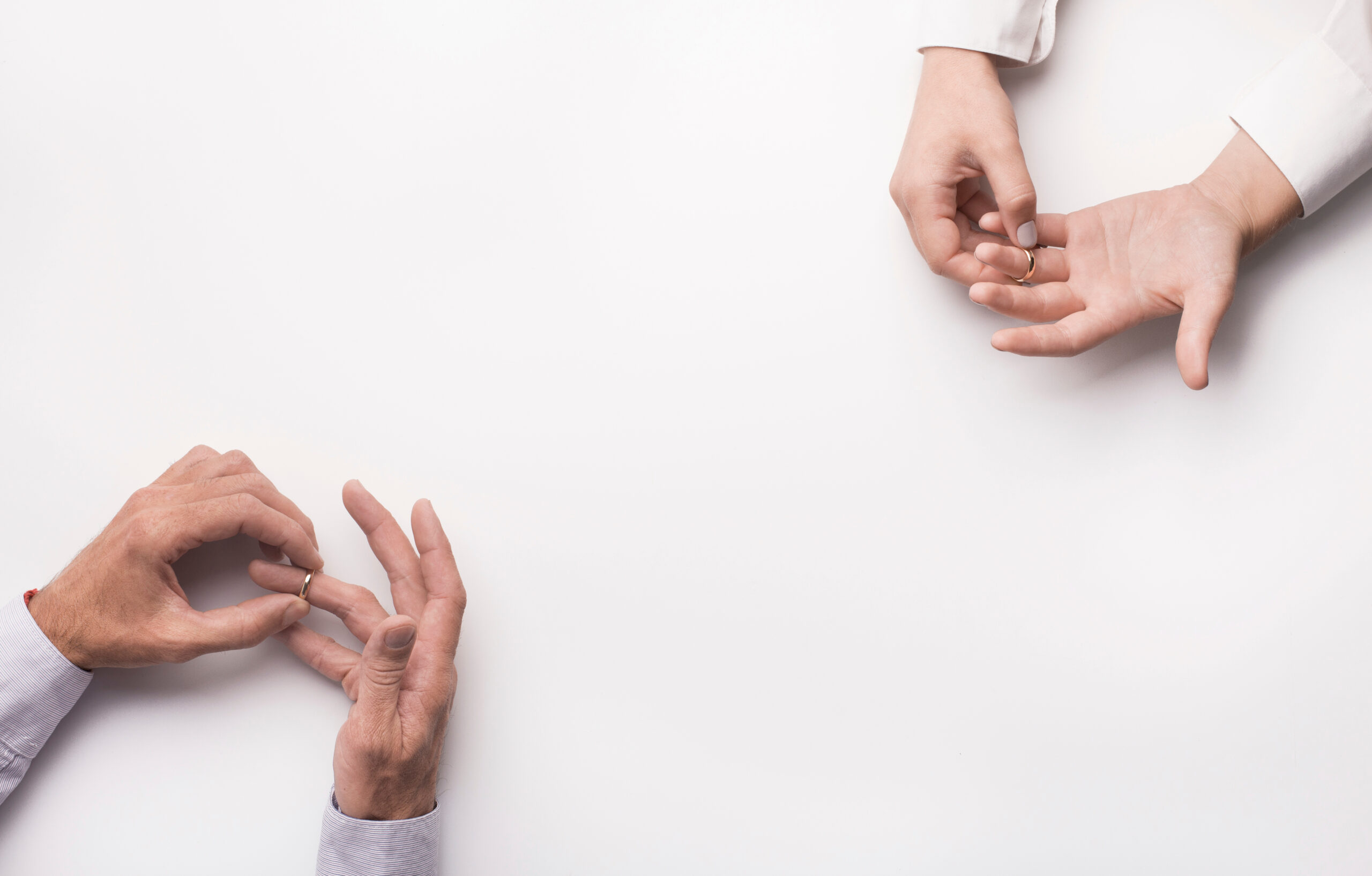 Mutual decision on divorce. Couple husband and wife taking off wedding rings on white background, copy space