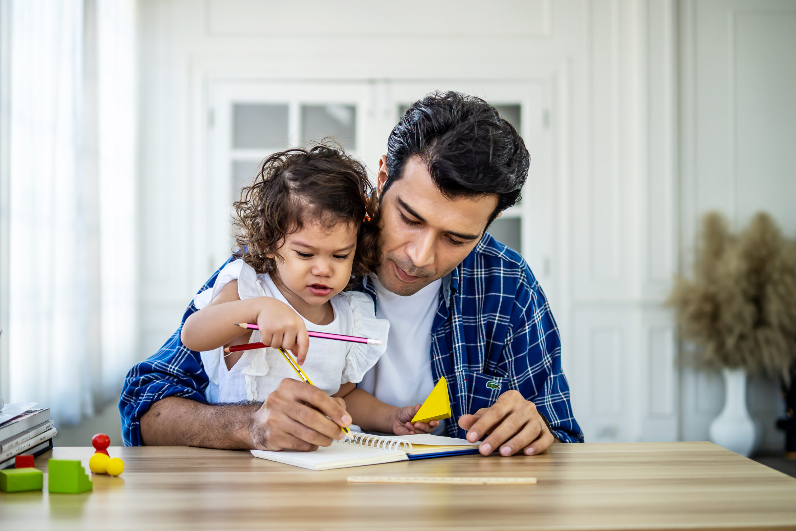 Portrait of young father teaching his cute little daughters' study. Excited smiling small child girl enjoying learning with pleasant dad at home. Children education, home schooling concept