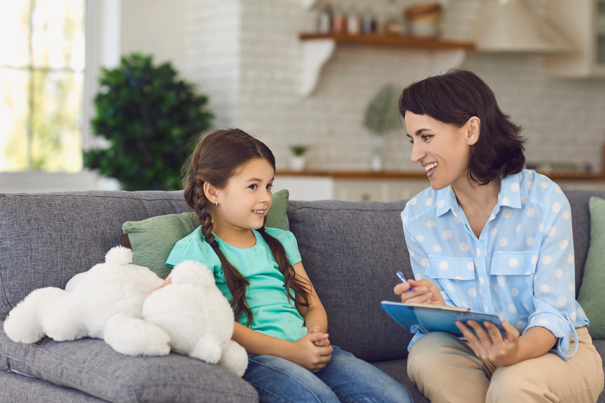 Relaxed smiling cute girl talking to a cheerful child psychotherapist during a therapy session in the office. Concept of trust and children's language therapy.