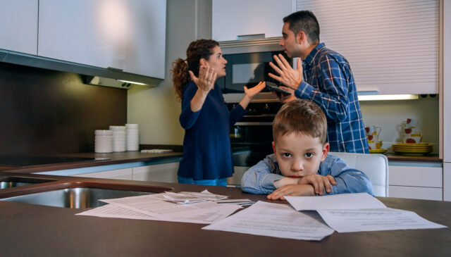 Sad boy looking at camera while his parents argue in the kitchen