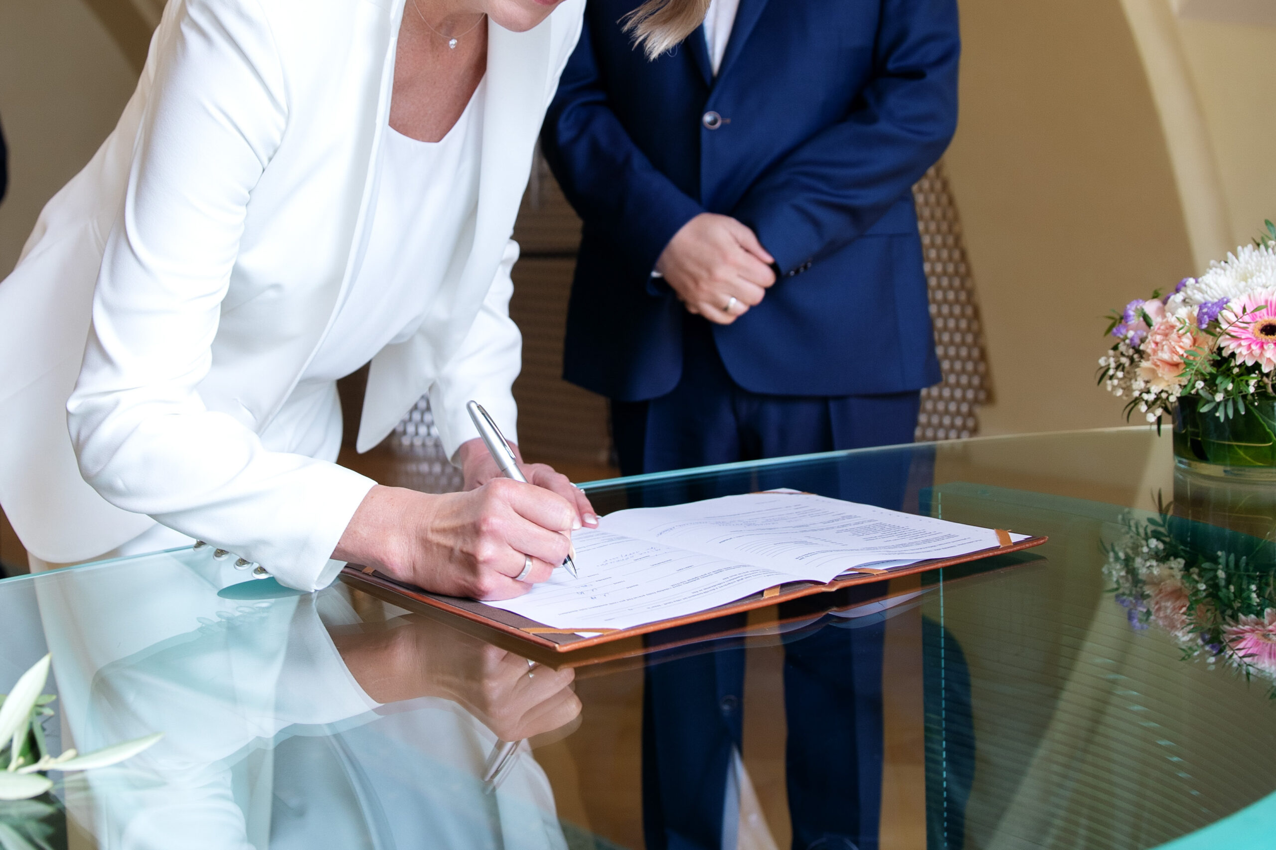bride and groom signing marriage agreement at desk. Woman's hand holding pen and signing paper document.